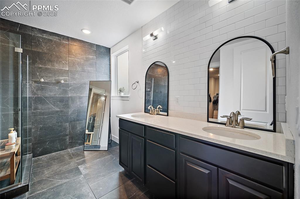 Image 30 of 46: Full bath featuring double vanity, a tile shower, tile walls, and recessed