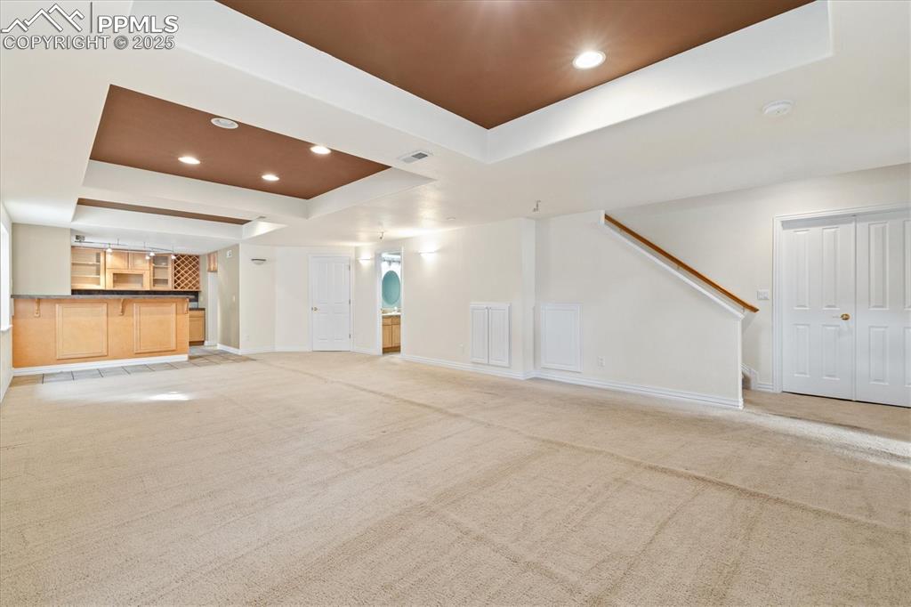 Image 24 of 33: Unfurnished living room featuring a tray ceiling, light carpet, recessed li
