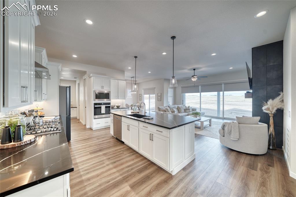 Image 13 of 50: Kitchen with white cabinets, a kitchen island with sink, light wood finishe