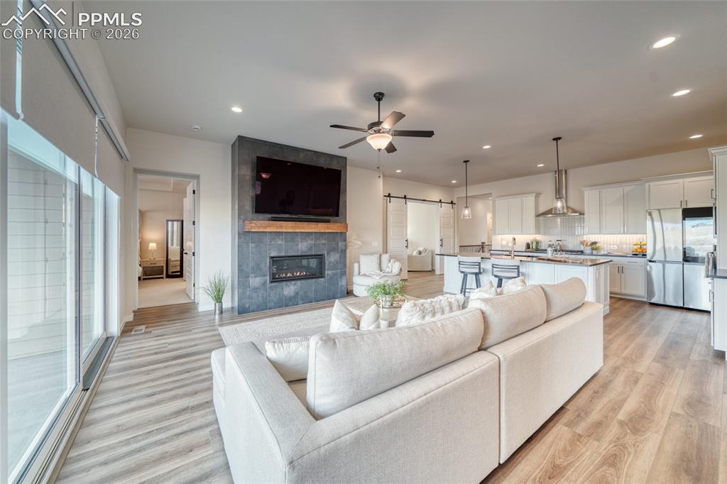 Image 23 of 50: Living area with a barn door, ceiling fan, a tile fireplace, light wood-sty