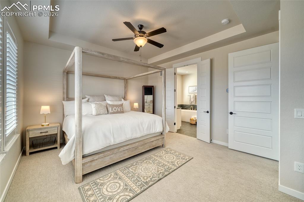 Image 35 of 50: Bedroom with a tray ceiling, light colored carpet, ensuite bathroom, and ce