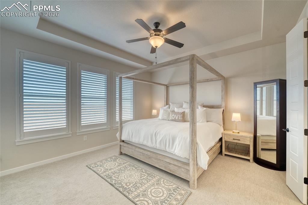 Image 36 of 50: Bedroom with a tray ceiling, light colored carpet, and ceiling fan