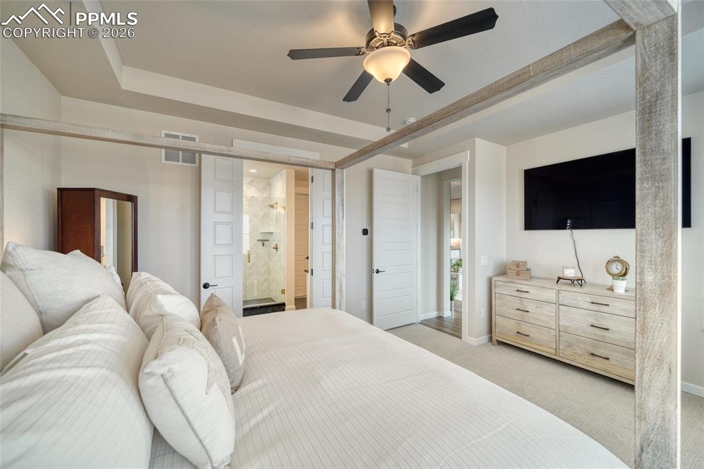 Image 37 of 50: Bedroom featuring a tray ceiling, light carpet, a ceiling fan, and ensuite 