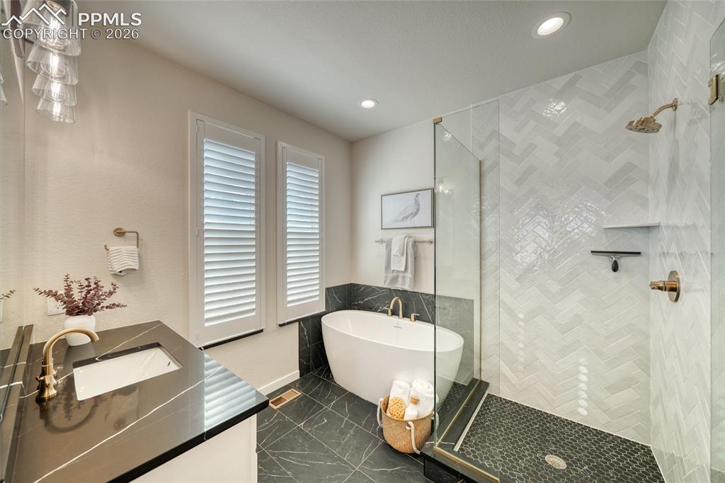 Image 38 of 50: Full bath featuring double vanity, a freestanding tub, a shower stall, rece