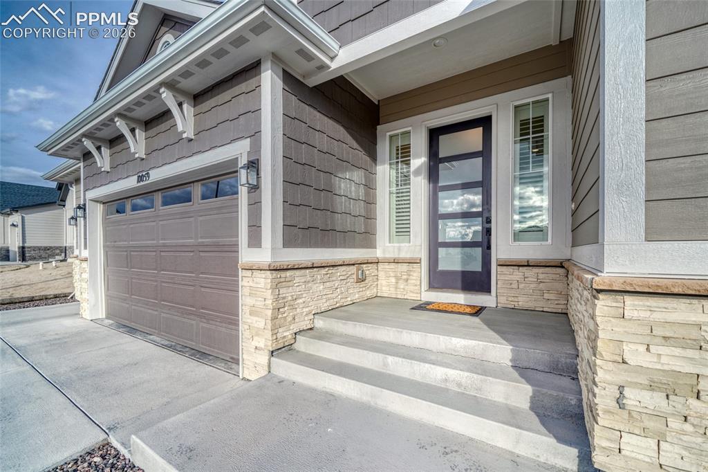 Image 8 of 50: View of exterior entry with stone siding, covered porch, driveway, and an a
