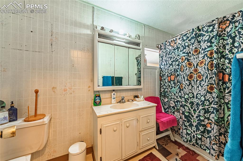 Image 11 of 22: Front Unit, Bathroom with tile walls, vanity, a textured ceiling, and a sho