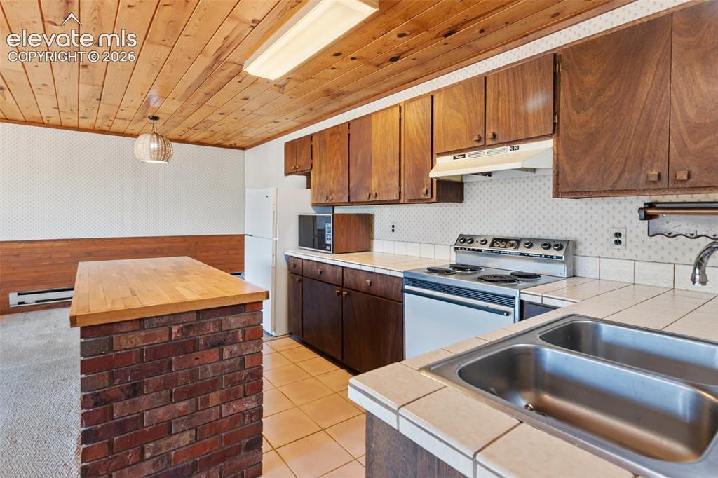 Image 16 of 46: Kitchen featuring wood-paneled ceiling, dark wood-finish cabinetry, a white