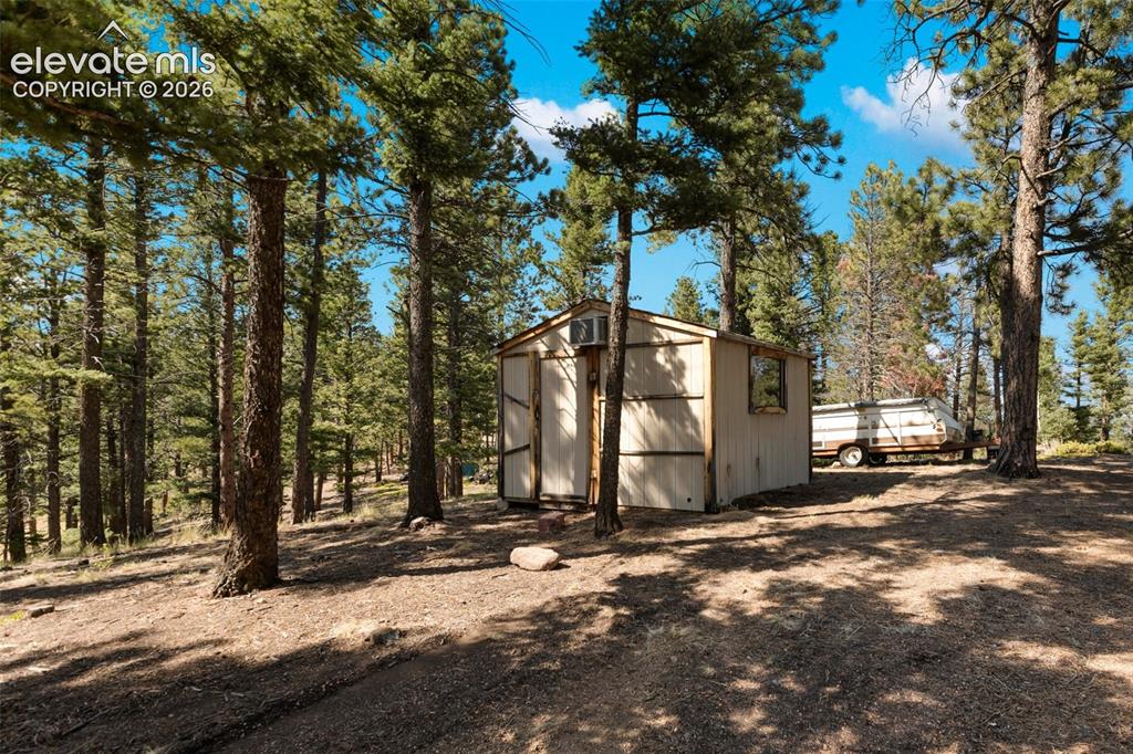 Image 28 of 46: Wooded lot featuring a compact structure with vertical siding and a single