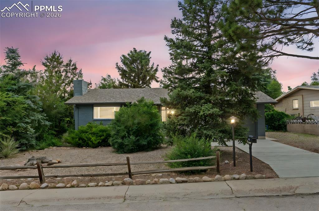 Caption: Obstructed view of property featuring a chimney, concrete driveway, a fenced front yard, and a garag