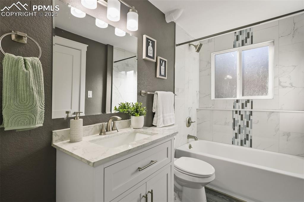 Image 13 of 15: Bathroom featuring a textured wall, vanity, and  shower combination