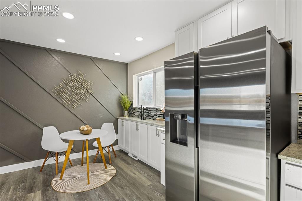 Image 4 of 15: Kitchen with stainless steel fridge, white cabinetry, dark wood finished fl