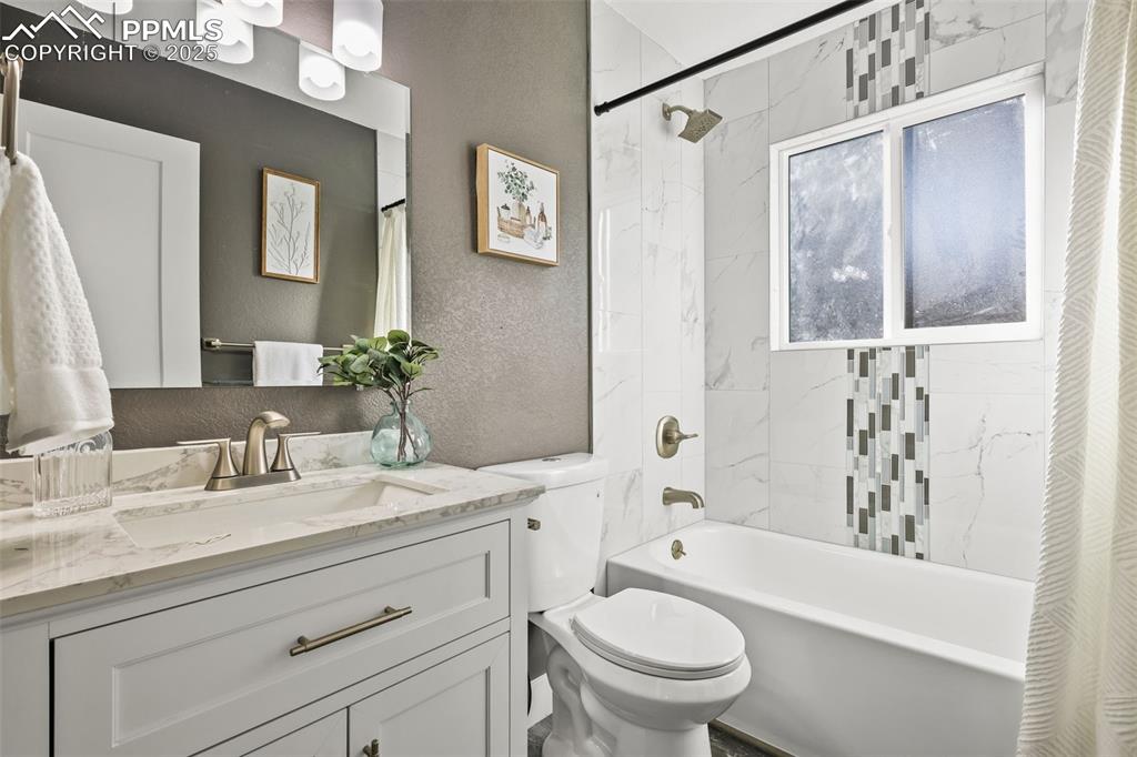 Image 8 of 15: Full bathroom with a textured wall, shower / tub combo with curtain, and va