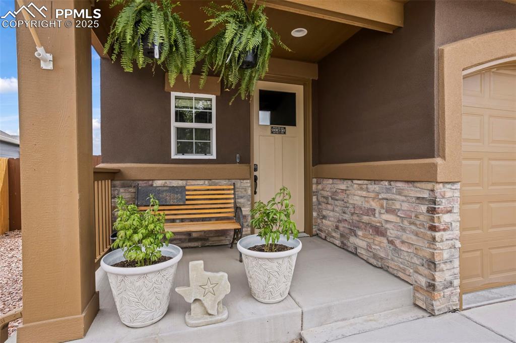 Image 18 of 45: Property entrance featuring stucco siding, a garage, covered porch, and sto