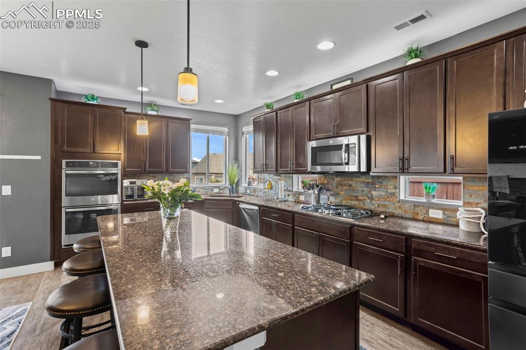 Image 23 of 45: Kitchen with stainless steel appliances, dark stone countertops, dark brown