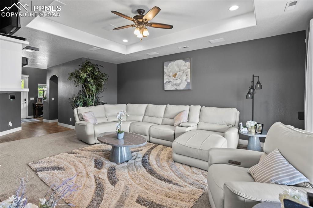 Image 27 of 45: Living room with ceiling fan, a raised ceiling, baseboards, arched walkways