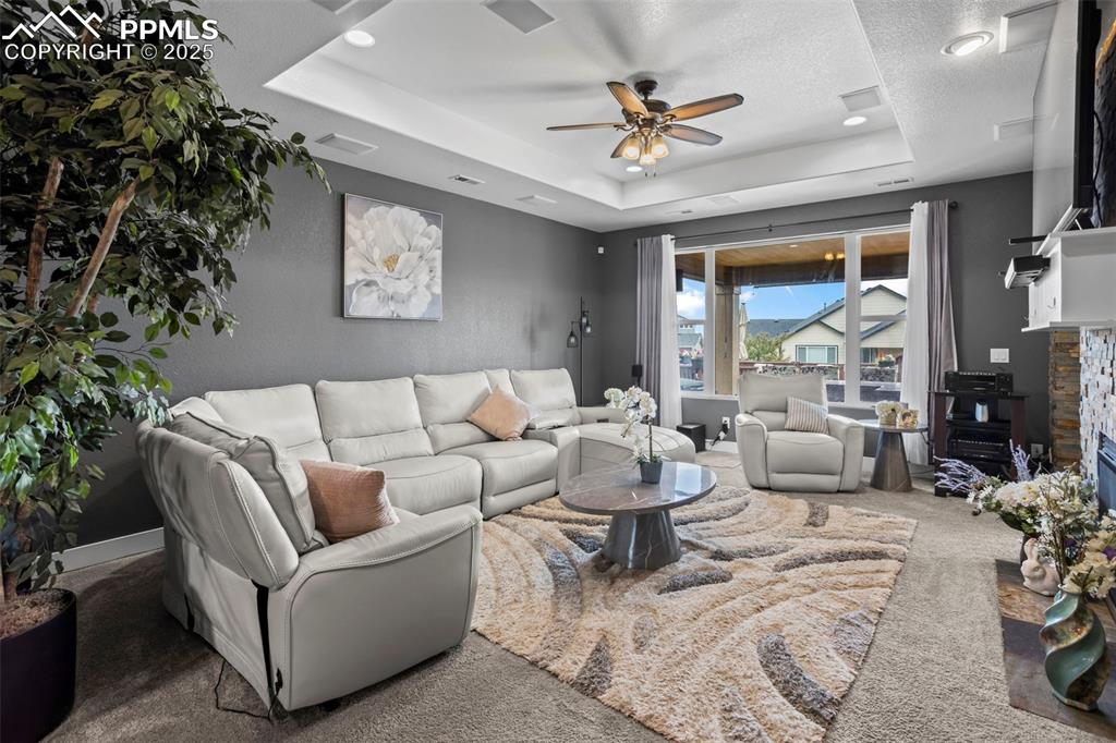 Image 28 of 45: Carpeted living room with a tray ceiling, ceiling fan, and a textured ceili