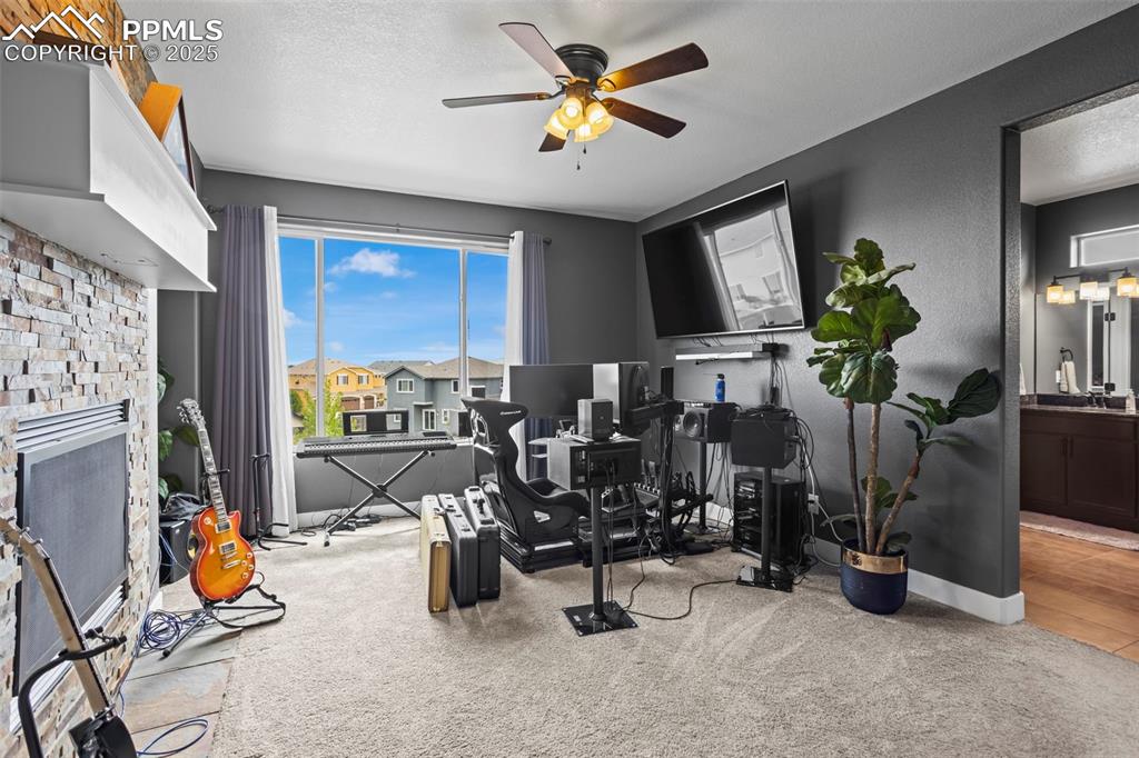 Image 42 of 45: Exercise area with a ceiling fan, carpet, a stone fireplace, baseboards, an