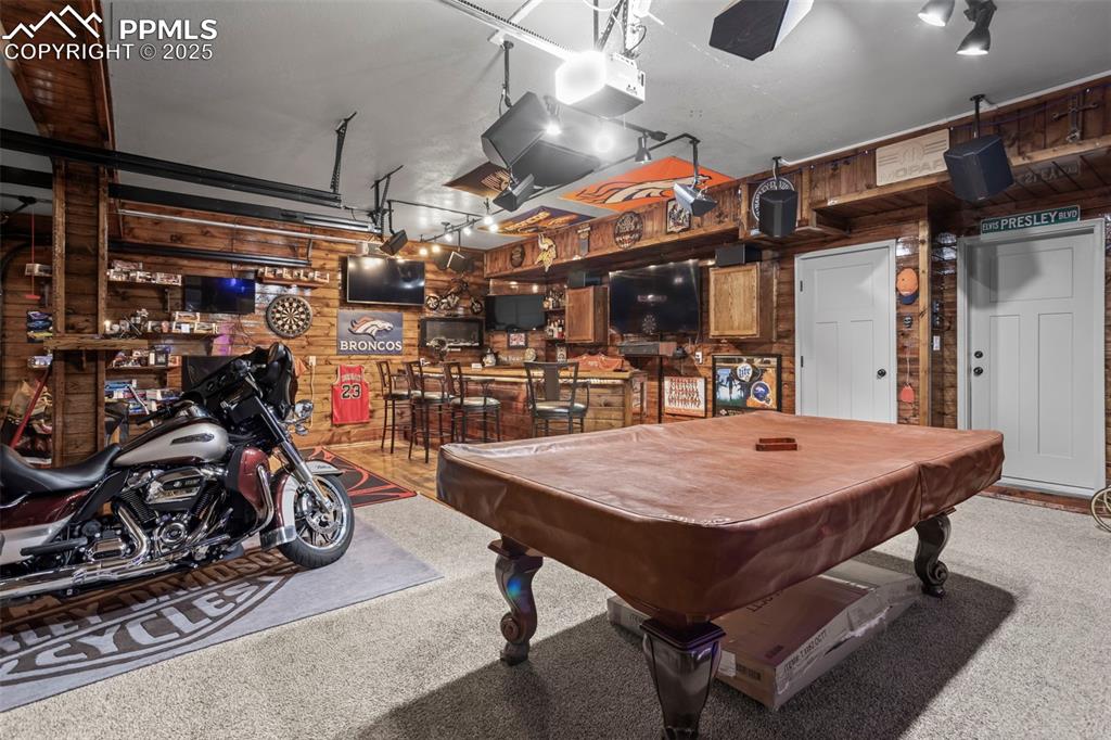 Image 44 of 45: Game room featuring wooden walls, billiards table, carpet, and a garage