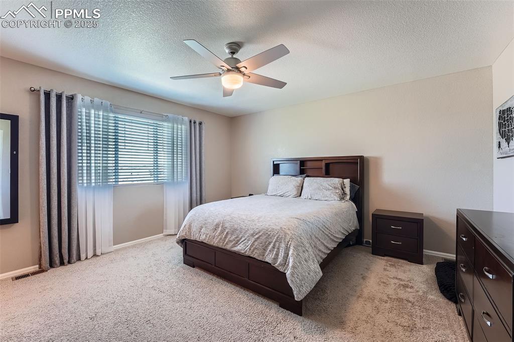 Image 17 of 32: Primary Bedroom featuring light carpet, a textured ceiling, and a ceiling f