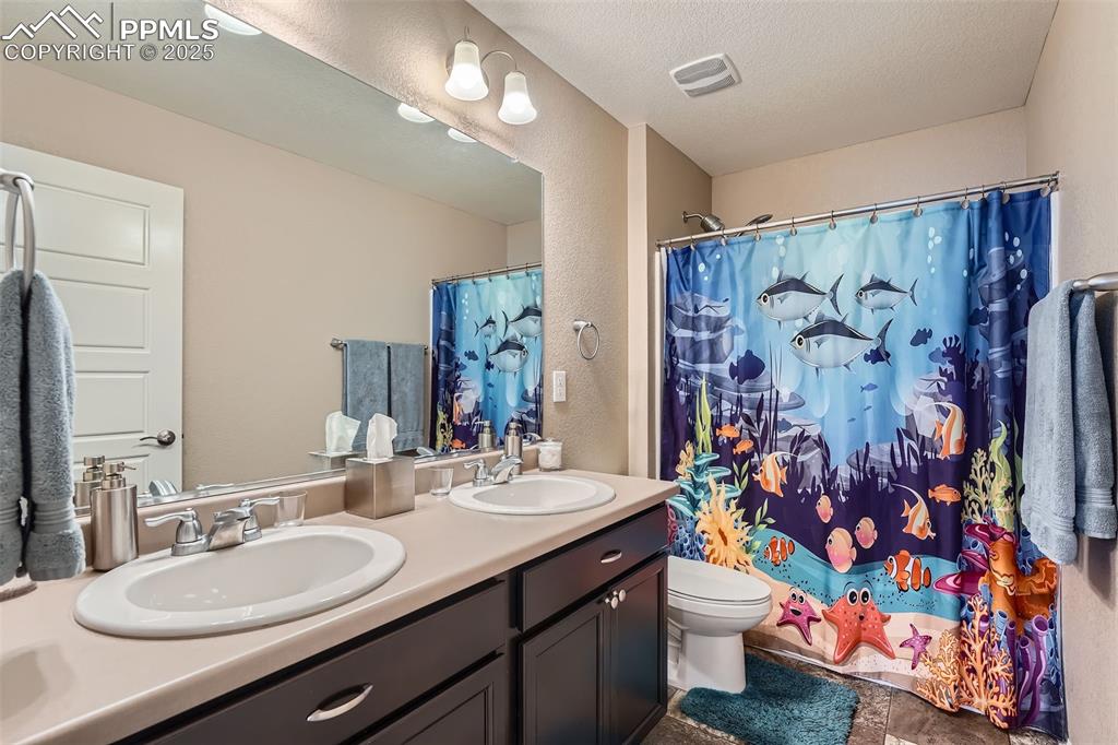 Image 25 of 32: Bathroom featuring double vanity, curtained shower, a textured ceiling, and