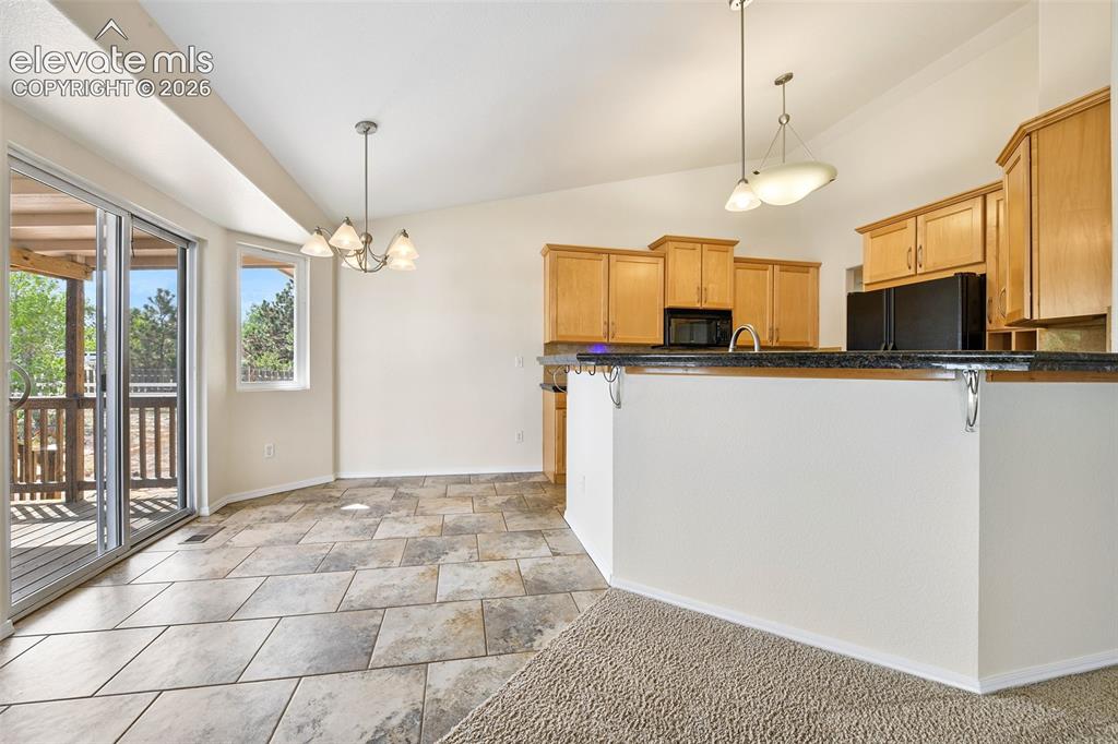 Image 10 of 50: Vaulted ceilings, a full kitchen with wood cabinetry, and sleek black appli