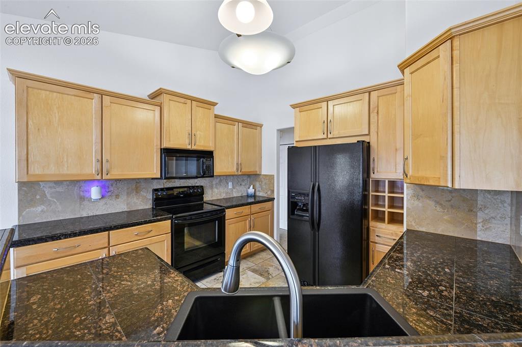 Image 12 of 50: Kitchen featuring light wood cabinetry, dark speckled countertops, stone-fi