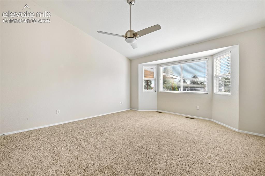 Image 17 of 50: Vaulted ceiling, bay window, light-colored carpeting, and a ceiling fan