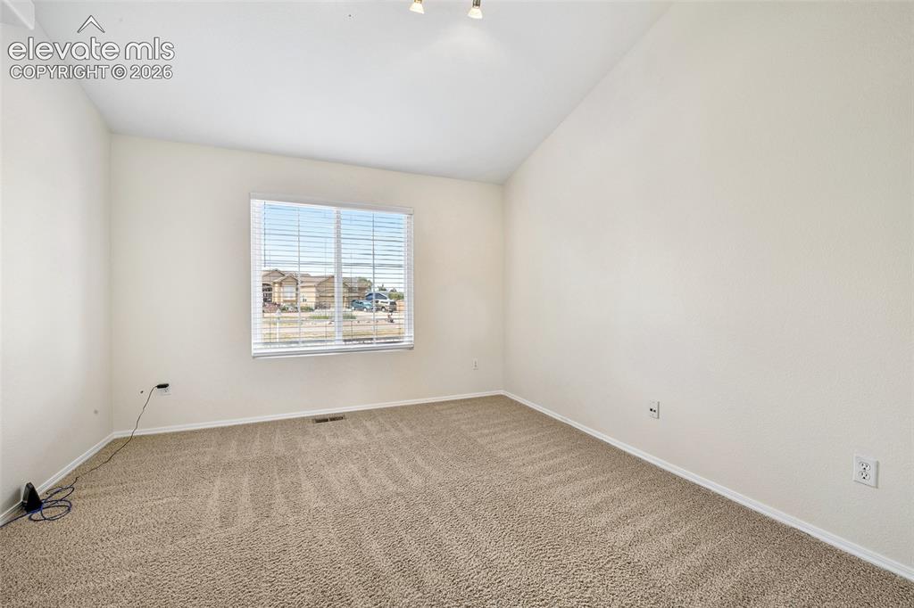 Image 20 of 50: Vaulted ceiling, neutral wall paint, carpeted flooring, and a window with b