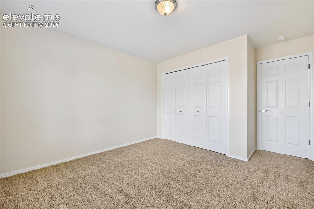 Image 22 of 50: Textured carpeting, neutral wall paint, white bi-fold closet doors, and a p