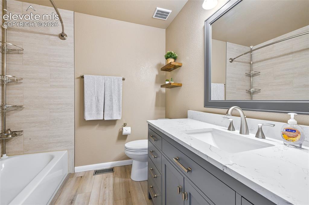 Image 23 of 50: White bathtub with tile surround, wood-finish flooring, and a gray vanity w