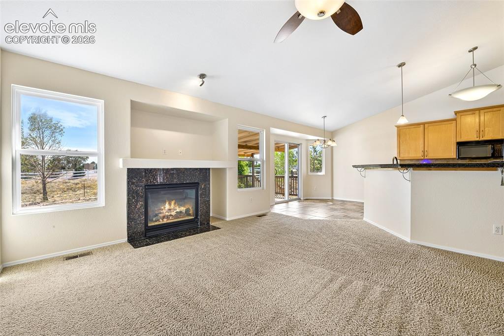 Image 8 of 50: Living area featuring a fireplace with a dark stone surround, a ceiling fan