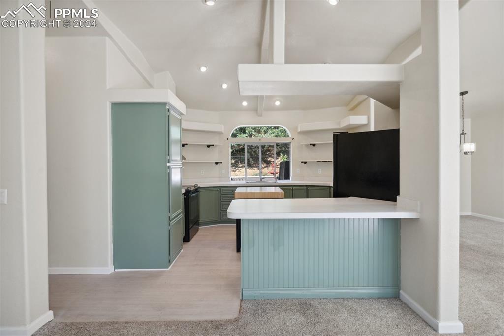Image 13 of 32: Kitchen featuring green cabinetry, black appliances, kitchen peninsula, and