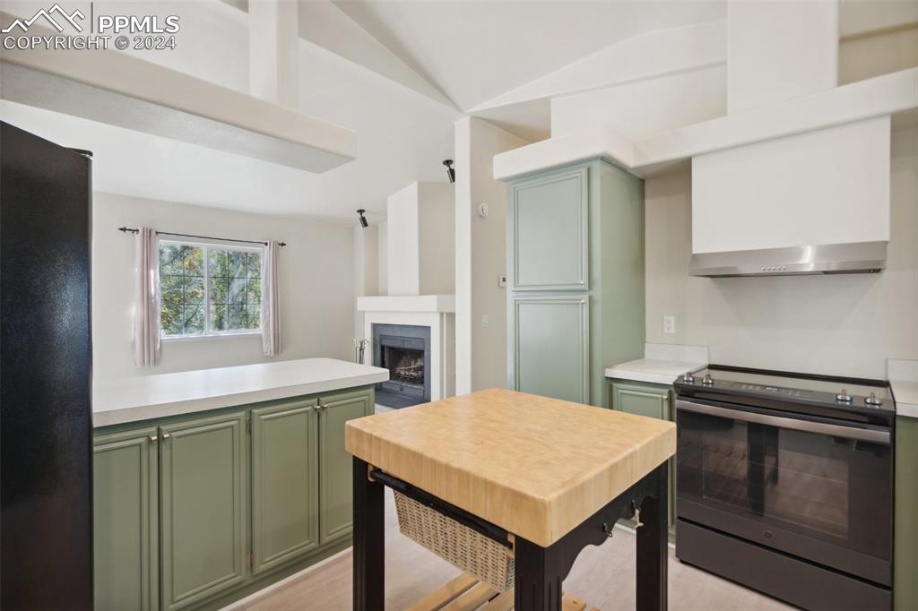 Image 17 of 32: Kitchen with vaulted ceiling, black refrigerator, light hardwood / wood-sty
