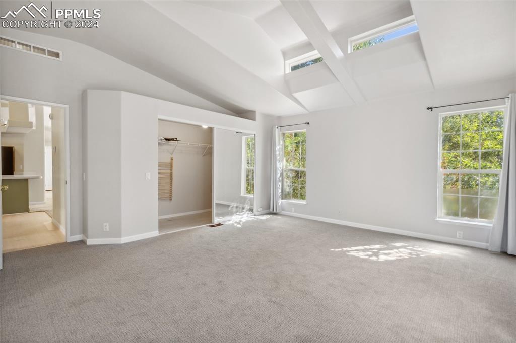 Image 28 of 32: Empty room with vaulted ceiling with beams, carpet flooring, and plenty of