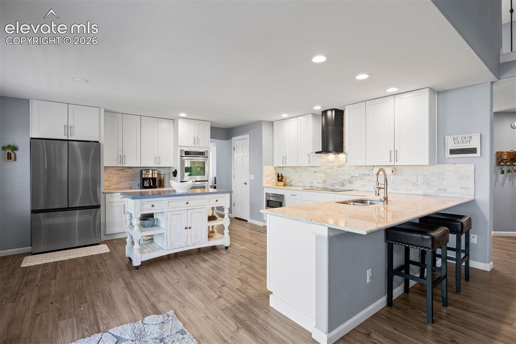 Image 14 of 50: Open-concept kitchen featuring wood-finish flooring, white cabinetry, stain