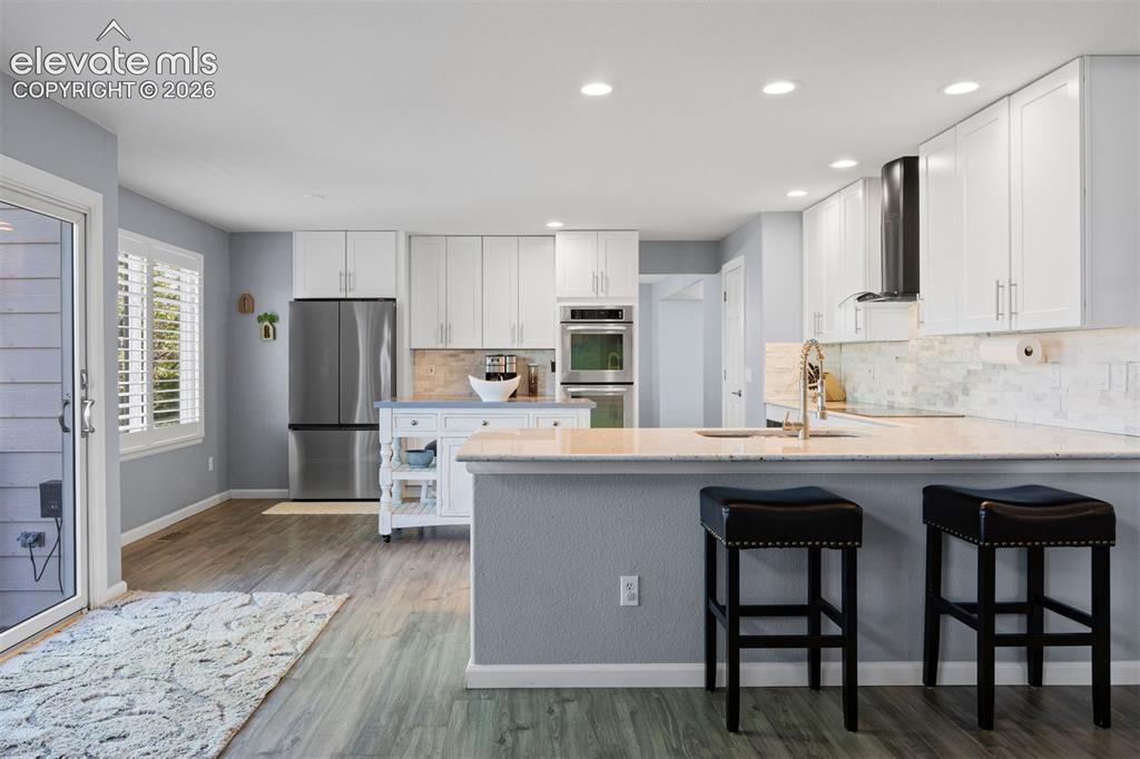 Image 15 of 50: Contemporary kitchen featuring light wood-finish flooring, white cabinetry,