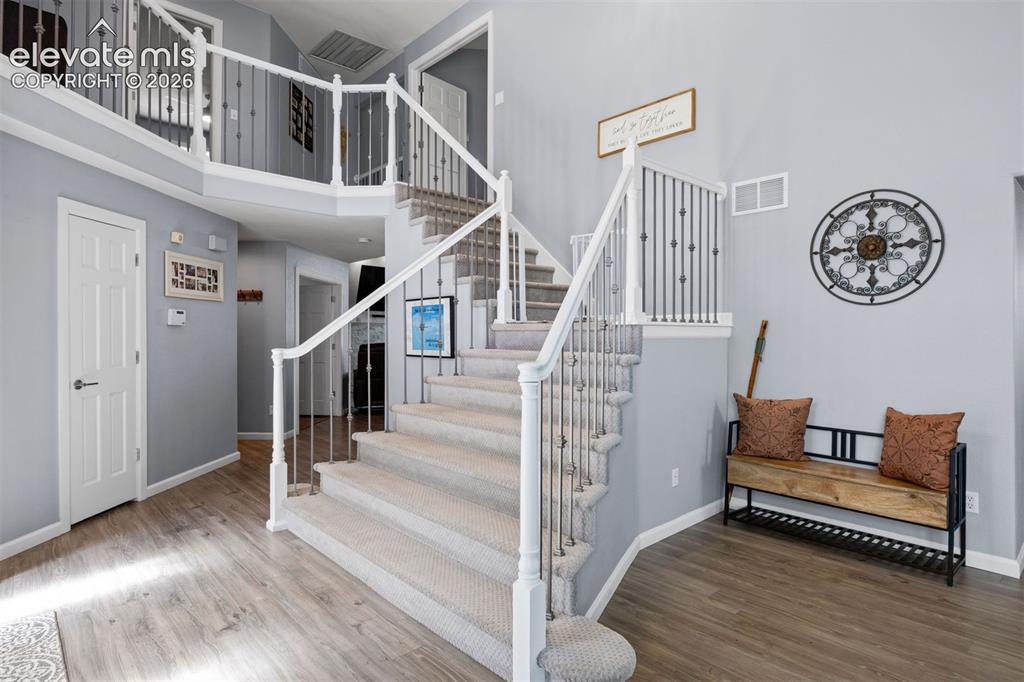 Image 26 of 50: Two-story entryway featuring wood-finish flooring, a carpeted staircase wit