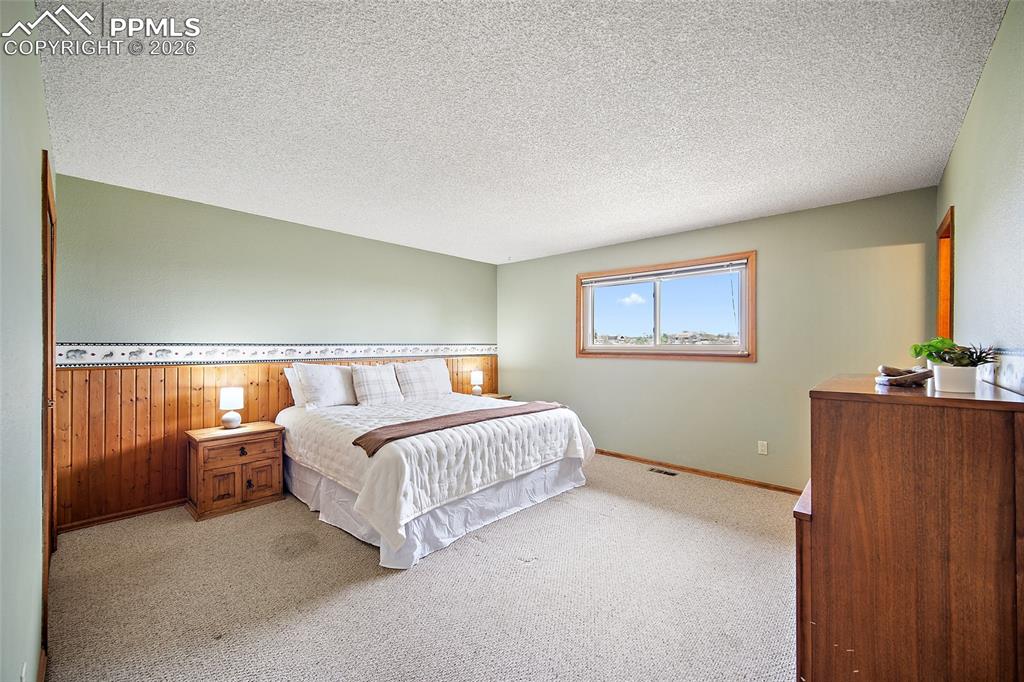 Image 15 of 40: Bedroom featuring a textured ceiling, light colored carpet, and wooden wall