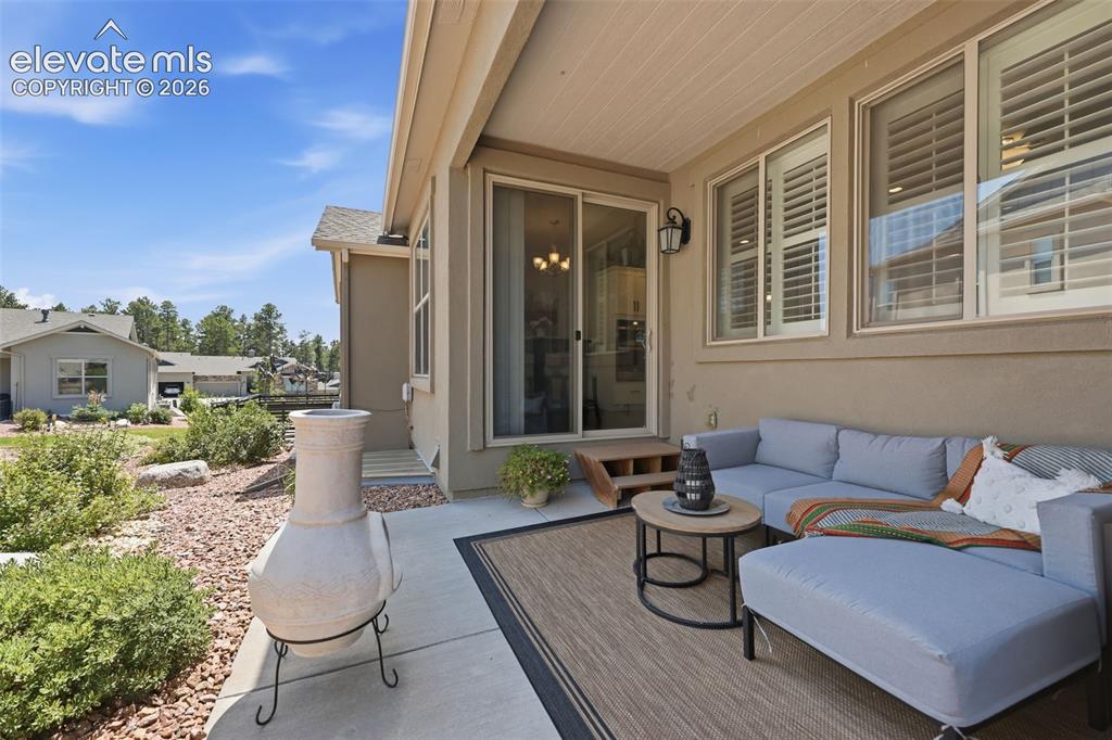Image 34 of 43: Covered outdoor patio with a stucco exterior and white window shutters.