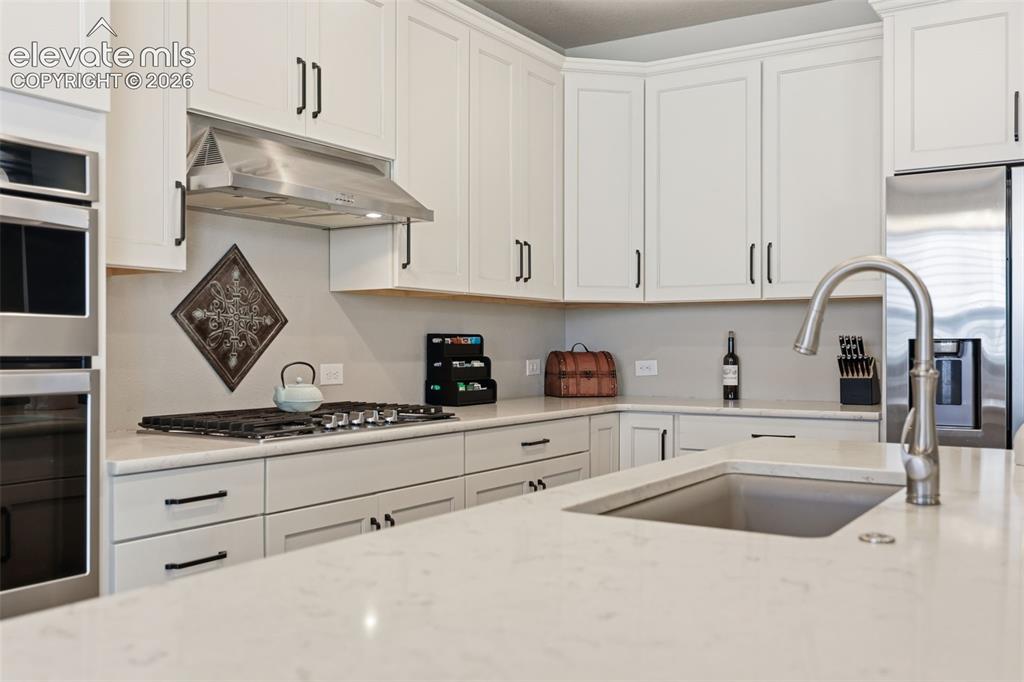 Image 5 of 43: White shaker-style cabinetry, stainless steel appliances, light color stone