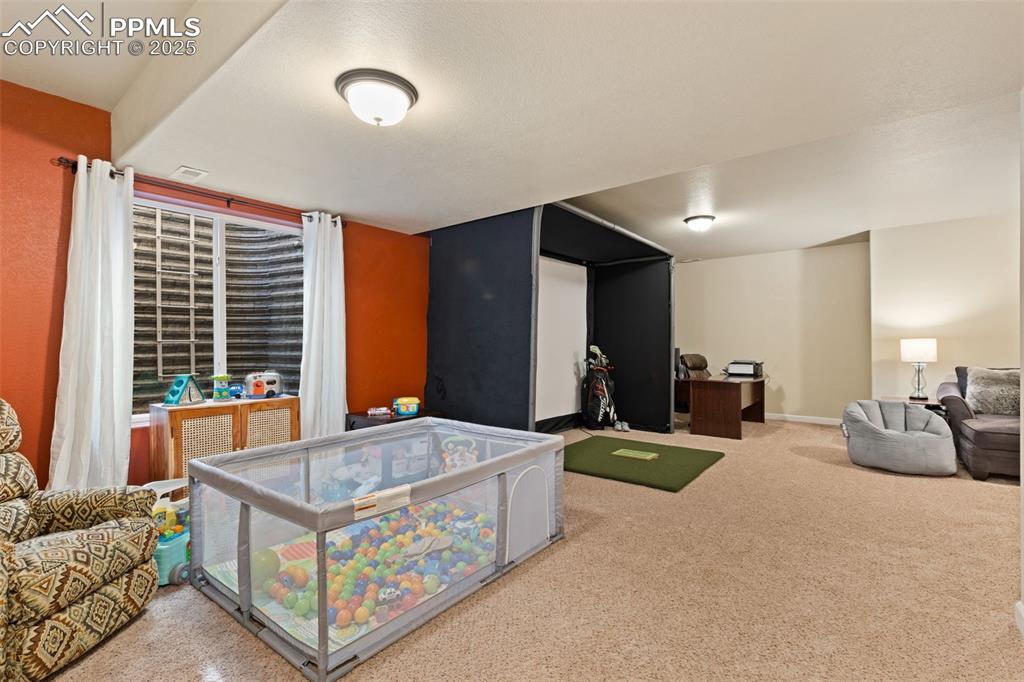 Image 24 of 31: Basement with golf simulator and carpet floors