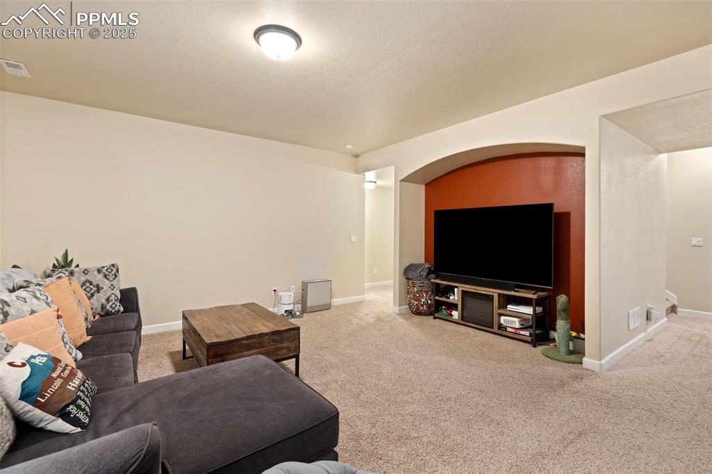 Image 26 of 31: Living area featuring carpet floors, a textured ceiling, and arched walkway