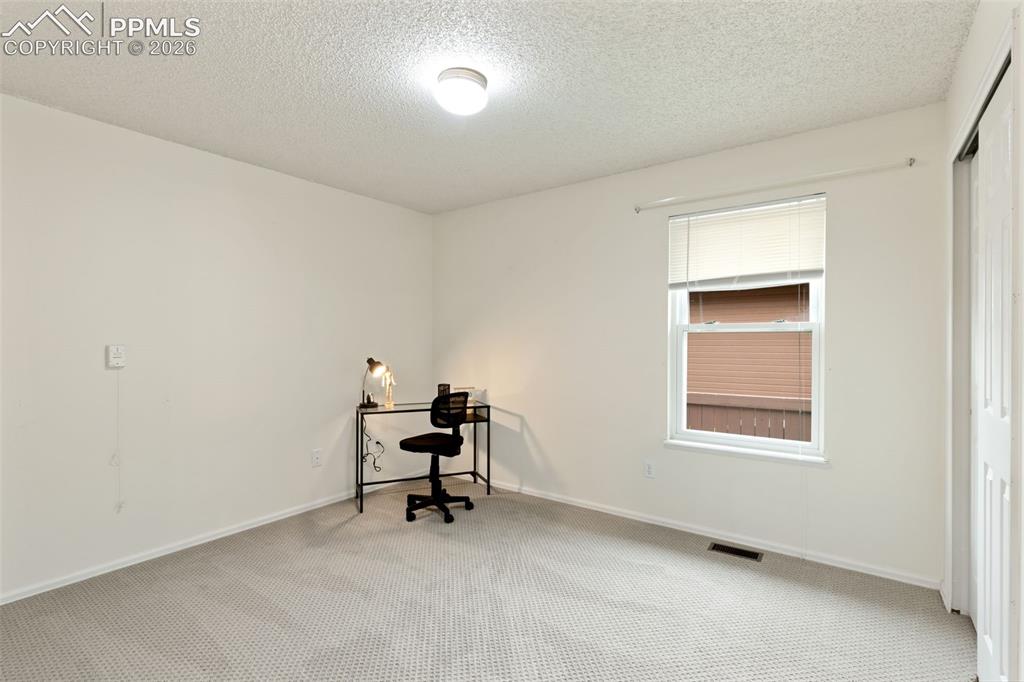 Image 10 of 27: The property features light-colored carpet flooring, a window with blinds,