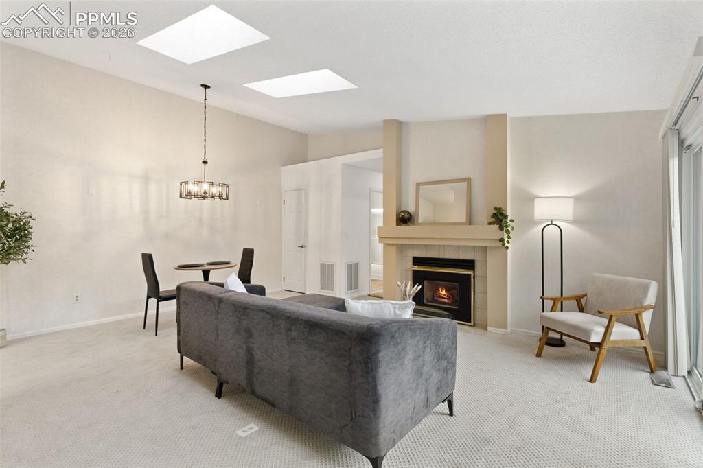 Image 4 of 27: The living area features a fireplace with a mantel, a vaulted ceiling with