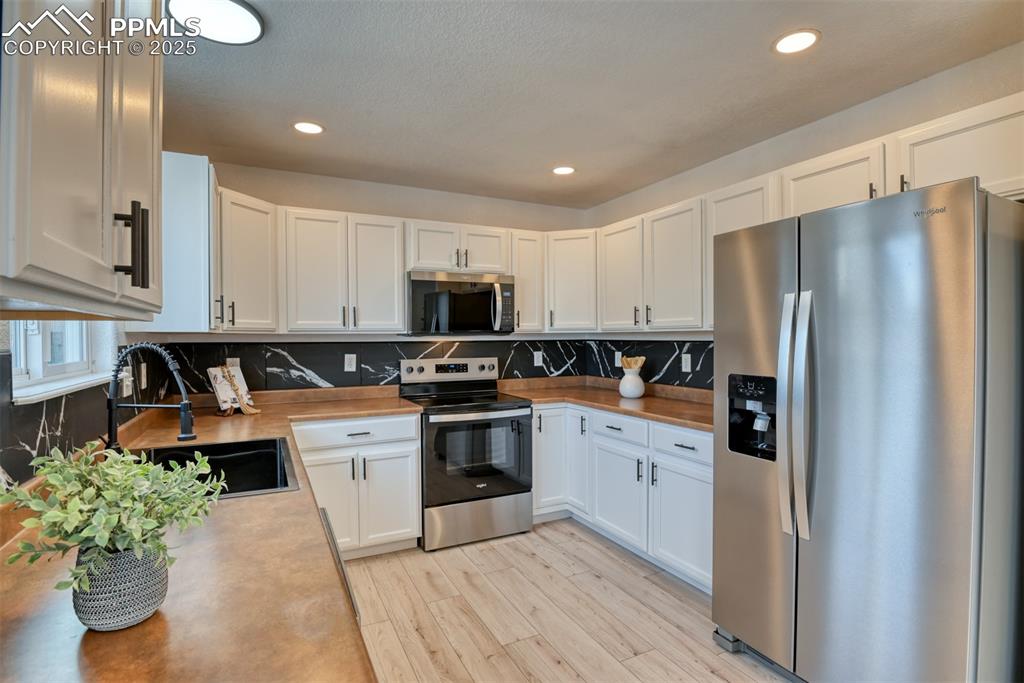 Image 10 of 45: Kitchen with stainless steel appliances, white cabinets, recessed lighting,