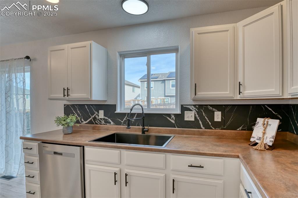 Image 12 of 45: Kitchen featuring dishwasher, decorative backsplash, white cabinets, a text