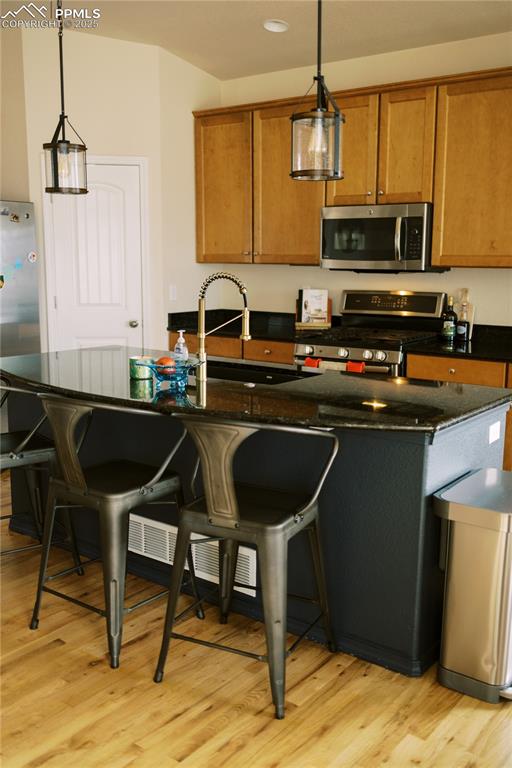 Image 15 of 36: Kitchen with brown cabinetry, appliances with stainless steel finishes, lig