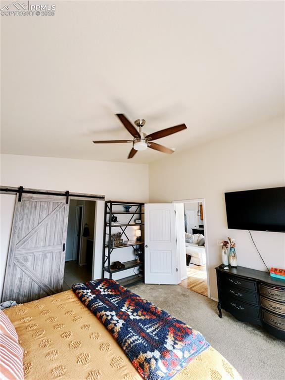 Image 19 of 36: Carpeted bedroom with ceiling fan and a barn door