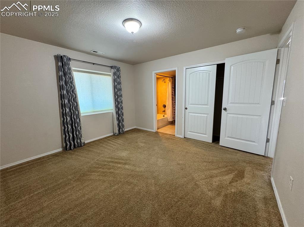 Image 30 of 36: Unfurnished bedroom featuring carpet flooring, a textured ceiling, ensuite 