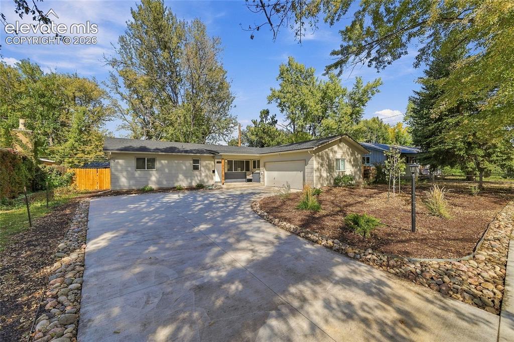 Caption: Expansive concrete driveway, attached garage, well-maintained exterior, mature landscaping, and deco